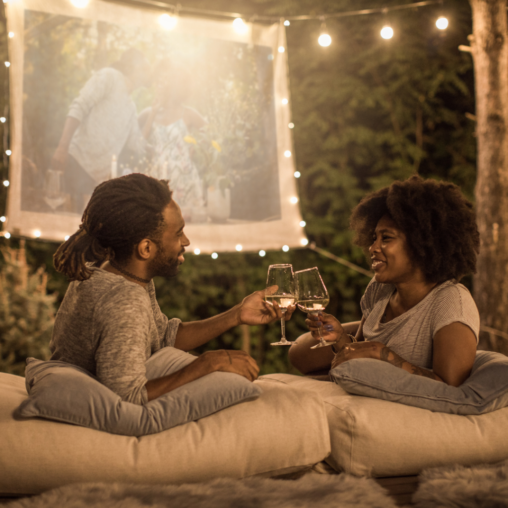 Couple enjoying a romantic backyard picnic with wine while displaying a beautiful image of a memory together on a projector screen. 
